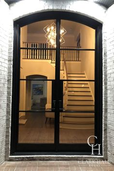 an open glass door leading to a staircase in a house with white brick walls and black doors