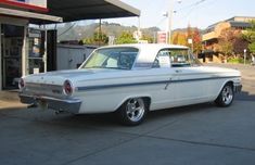 an old white car parked in front of a gas station