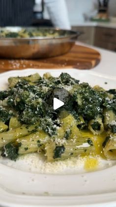 a white plate topped with pasta and spinach covered in cheese on top of a table