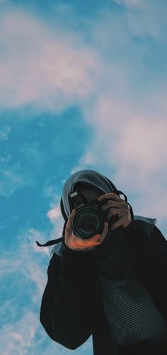 a person holding a camera up to their face in front of a blue sky with clouds