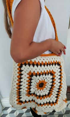 a woman carrying a crocheted bag with an orange and white design