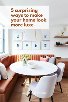 a dining room table with white chairs and a bench in front of the window that has pictures on the wall above it