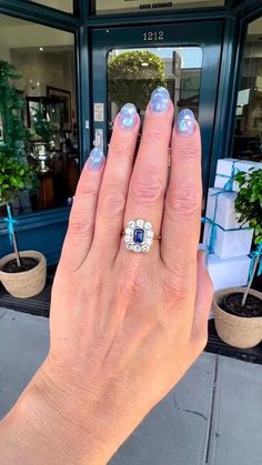 a woman's hand with blue and white nail polish holding an engagement ring in front of a store