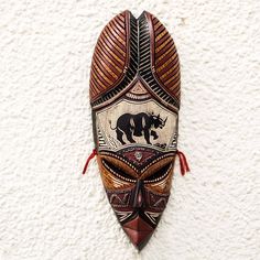 an african mask hanging on the wall with a rhinoceros design painted on it