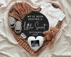 a heart shaped basket filled with baby items on top of a white bed covered in blankets