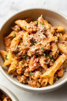 two bowls filled with pasta and meat covered in sauce on top of a white table