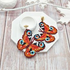 Embrace the beauty of nature with the Majestic Peacock Butterfly Earrings. These striking earrings feature a vivid design inspired by the peacock butterfly, meticulously crafted using high-quality Japanese Delica beads. The bright orange tones and intricate patterns make these earrings a captivating addition to any jewelry collection. Finished with 18K gold-filled studs, these large, eye-catching earrings are perfect for those who appreciate unique, bold accessories. Whether you're dressing up for a special occasion or looking to elevate your everyday style, these earrings are sure to draw compliments and admiration for their stunning artistry. Materials: Japanese beads, 18K gold-filled studs Height of butterfly: 1 7/8 inches ( 4.8 cm ) The width at the top: 2 1/8 inches ( 5.5 cm ) ● ● ● D Peacock Butterfly, Beaded Earrings Native, Beaded Art, Japanese Beads, Orange Tones, Bold Accessories, The Peacock, Butterfly Jewelry, Delica Beads