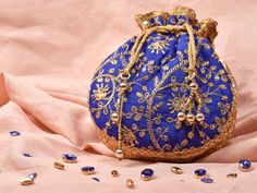 Blue Potli Bag with Pearl Handle Strap With its classy zari work and a pearl handle strap all in gold this Blue Potli Bag is ideal for this wedding season. Fabric Raw Silk Color Royal Blue Embroidery Zari Work in Gold Size amp Dimensions Height - 8 inWidth - 7.5 inDepth - 1.5 in Strap Pearl Handle Strap Closure Tasseled Drawstring Compartments Single compartment Care Wipe with a soft clean amp dry cloth to remove dust When not in use store it in a dust bag for longer product life Avoid liquid ex Bridal Mask, Potli Bag, Ethnic Bag, San Ramon, Potli Bags, Royal Blue And Gold, Zari Work, Blue Embroidery, Gold Work