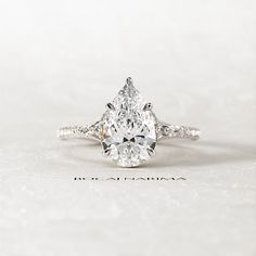 a pear shaped diamond ring on top of a white surface with the word love written below it