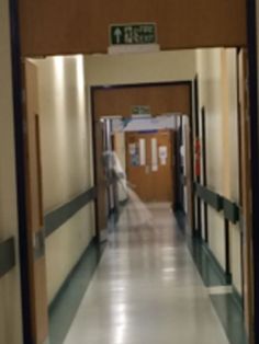 an empty hospital hallway with the door open and people walking down one side of the corridor