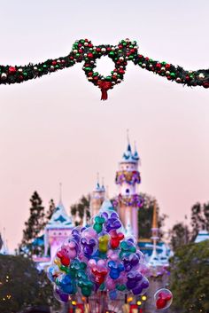 balloons are being flown in front of the castle at disneyland world, during christmas time