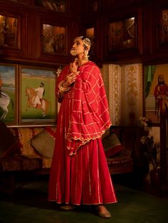 Enter the world of luxurious & regal clothing with Sahiba. Celebrate the grandeur of beauty, celebrations, dressing up and womanhood with vintage textiles and silhouettes. Set of 3 consists of Kalidar, pajama and dupatta. Kurta: A red ghera cotton kalidar is adorned with heavy gold gota work on neck and kalis. Dupatta: A handspun mul red dupatta is detailed with zari and mirror scallop detailing with heavy gota chaukadi work Bottom: Red Farshi pajama is detailed with pure metal gold lampi. Mater Red Designer Wear Sets With Traditional Drape, Red Traditional Drape Sets For Designer Wear, Red Palazzo Set With Dabka In Traditional Drape, Festive Kurta With Cutdana And Traditional Drape, Red Sharara With Straight Kurta For Traditional Ceremonies, Red Straight Kurta Sharara For Traditional Ceremonies, Festive Cutdana Palazzo Set With Traditional Drape, Traditional Floor-length Chanderi Palazzo Set, Traditional Red Floor-length Palazzo Set