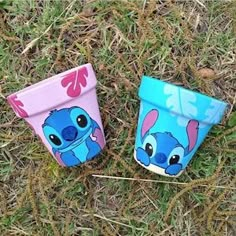 two plastic cups sitting in the grass with faces painted on them to look like stitchers