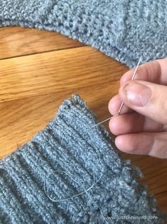 someone is stitching the ends of their sweaters together with scissors and thread on a wooden table