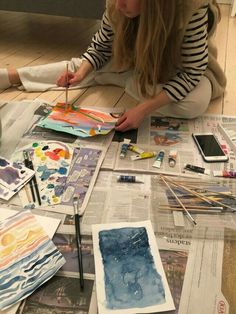 a woman is sitting on the floor working on some art work with watercolors