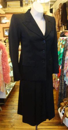 This is a black wool gabardine suit from the early 1940's.  It features a fitted jacket with medium wide notched lapels and a wide shoulder line, and a skirt with 3 inverted pleats in the front and the back. The skirt opens with a well working metal zipper.  The label is from Schmitt's Clothier's in Milwaukee.  The jacket is lined in black sateen.  There is hand done topstitching around the lapels.  I didn't find any problems or issues. It's in great condition!   Comes from a smoke free home.Mea Black Notch Lapel Skirt Suit For Business, Tailored Black Skirt Suit For Business, Classic Notch Lapel Skirt Suit For Career, Elegant Formal Wool Skirt Suit, Elegant Wool Skirt Suit For Formal Occasions, Tailored Classic Career Skirt Suit, Classic Black Business Skirt Suit, Classic Black Skirt Suit For Work, Classic Black Skirt Suit For Business