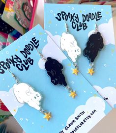 two black and white earrings with stars hanging from them on a blue card that says sorry dude doodle club