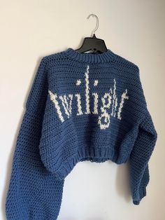 a blue sweater with white writing on it hanging from a hanger against a wall