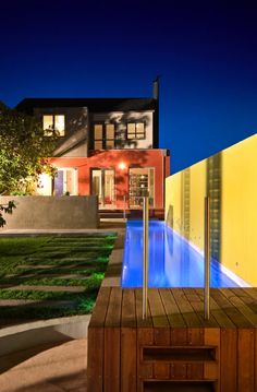 an outdoor hot tub in front of a large house with a swimming pool at night