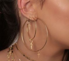 a woman wearing large gold hoop earrings with cross charms