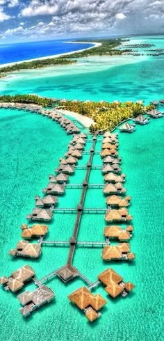 an aerial view of a resort in the ocean with thatched huts on stilts