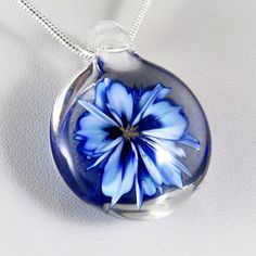 This unusual and unique pendant has a realistic blue and white glass 3D flower inside a solid glass - this isn't resin or a real flower, it's all made entirely of glass! I've used a cobalt blue over white, which I've graduated in tone and to form bands on the petals to make the flower look more realistic, also giving the edges and centre a darker rim of blue. In the centre I've added some yellow 'stamens' to make it look more realistic, where some bubbles have clustered around them to add a dew Blue Flower Necklace For Gifts, Blue Flower Necklace With Birth Flower Detail, Blue Flower Necklace Gift, Blue Birth Flower Necklace, Clear Flower Shaped Jewelry Gift, Blue Flower Charm Necklace As Gift, Blue Birth Flower Round Pendant Necklace, Blue Flower Pendant Jewelry As Gift, Blue Flower Pendant Necklace For Gift