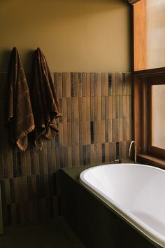 a bath tub sitting under a window next to a towel hanging on the side of it