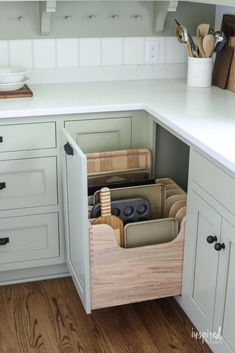 a kitchen with white cabinets and drawers filled with utensils in the bottom drawer