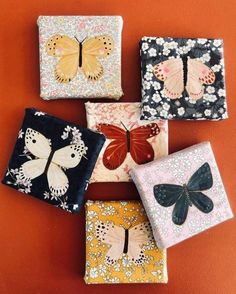 four small boxes with butterflies on them sitting next to each other in front of an orange wall