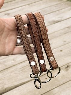 a hand holding three brown leather wristbands with metal rings on each one side