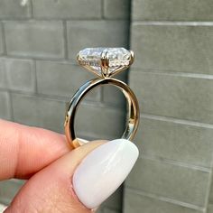 a woman's hand holding a diamond ring in front of a brick wall