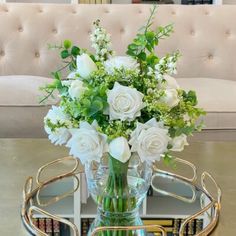 a glass vase filled with white flowers sitting on top of a table next to a couch