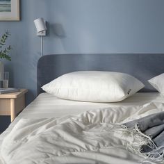 an unmade bed with white pillows and blankets on it, next to a night stand