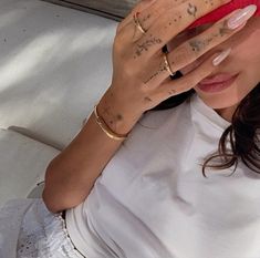 a woman with tattoos covering her face and holding her hand up to her head while sitting on a couch