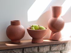 three clay vases sitting on top of a wooden shelf next to each other with apples in them