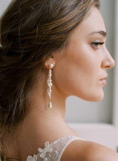 a woman wearing earrings with pearls on the back of her head and shoulder, looking off to the side