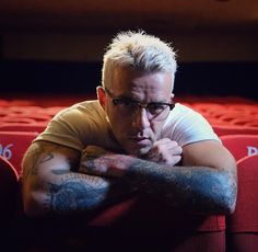 a man with tattoos on his arm sitting in a theater