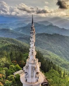 an aerial view of a tower in the middle of trees and mountains with clouds overhead