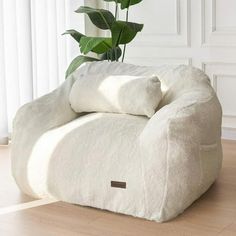 a large white chair sitting on top of a hard wood floor next to a potted plant