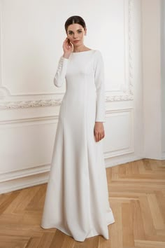 a woman in a long white dress standing on a wooden floor with her hand to her face