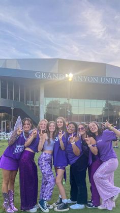 a group of girls posing in front of the grand canyon university building with their hands up