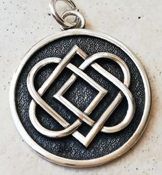 a silver pendant with an intertwined knot on the front and center circle in the middle