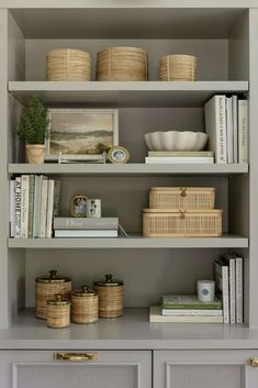 shelves with baskets, books and other items on them in a living room area that is painted light gray