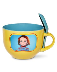 a yellow coffee cup with a blue handle and a cartoon character on the side, in front of a white background