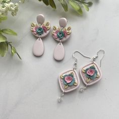 three pieces of jewelry sitting on top of a white table next to flowers and greenery