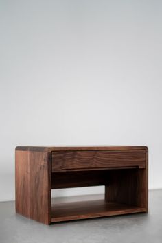 a small wooden table sitting on top of a cement floor next to a white wall