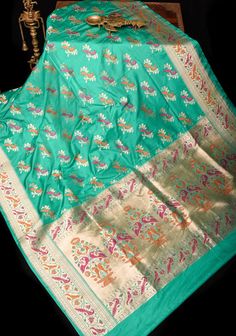 This teal Banarasi Katan silk saree with Meenakari Peacock design Motifs and Paithani style tissue and meena Borders and pallu add elegance and style to the overall look. Perfect for special occasions, this saree tells tall tales of craftsmanship! SILK MARK CERTIFIED This saree is ready to wear with fall and pico done. Handmade silk tassels adorn the pallu and add more grace to it. An unstitched blouse fabric is included. *Note: There may be minor variations in the shade, the texture of the product. Hues/textures show differently due to variations in screen settings and other factors, *Note: This is a handwoven saree and there may be slight inconsistencies such as in it's weaving. These are characteristic of handmade products and attest to their originality and are not considered as defect Luxury Peacock Design Saree For Puja, Luxury Saree With Peacock Design, Luxury Art Silk Saree With Peacock Design, Luxury Saree With Peacock Design For Puja, Luxury Katan Silk Dupatta With Peacock Design, Green Saree With Motifs For Festivals, Paithani Silk Saree With Meenakari, Green Katan Silk Saree With Motifs, Green Katan Silk Traditional Wear With Motifs