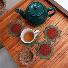 a tea pot sitting on top of a wooden table next to a crocheted coaster