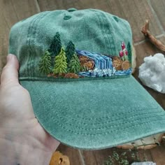 a person holding a green hat with trees on it and other items around the cap