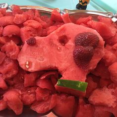 a metal bowl filled with sliced up watermelon and strawberries next to a toy